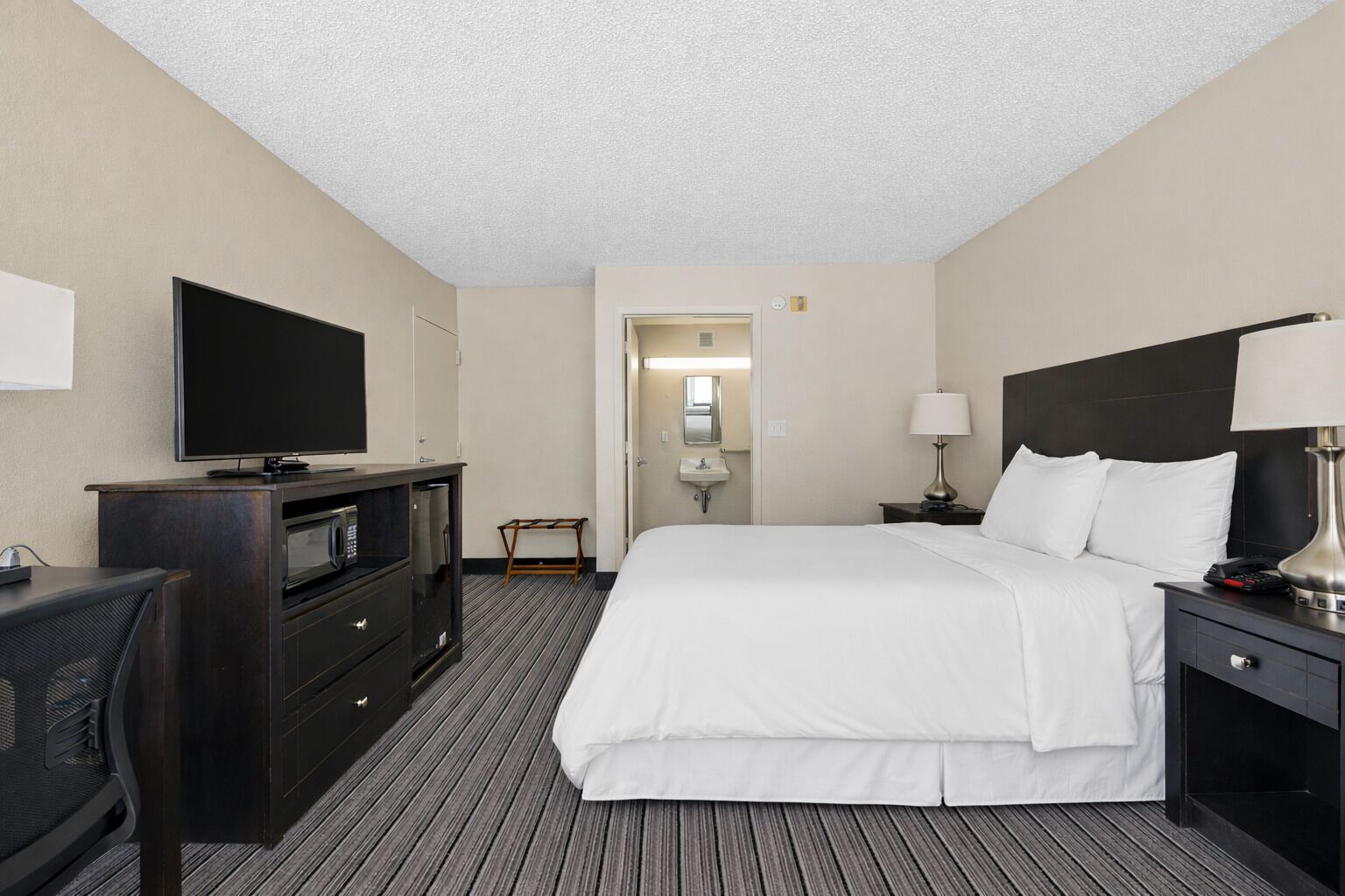 Habitación de hotel con cama, televisión, escritorio con computadora, lámpara y mesita de noche.