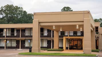 Un hotel de varios pisos con entrada cubierta, estacionamiento y un área ajardinada con un pequeño jardín.