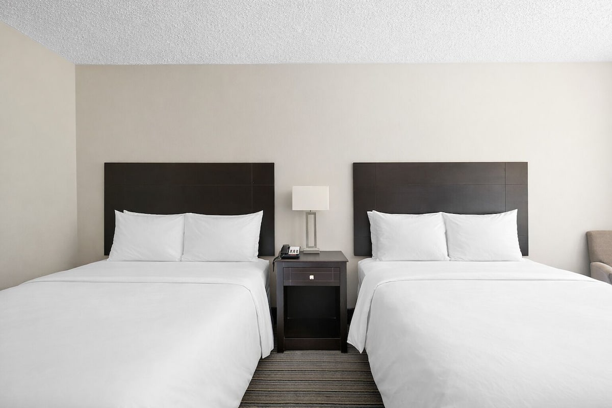 Hotellihuone, jossa on kaksi sänkyä, yöpöytä lampun kanssa ja tuoli.