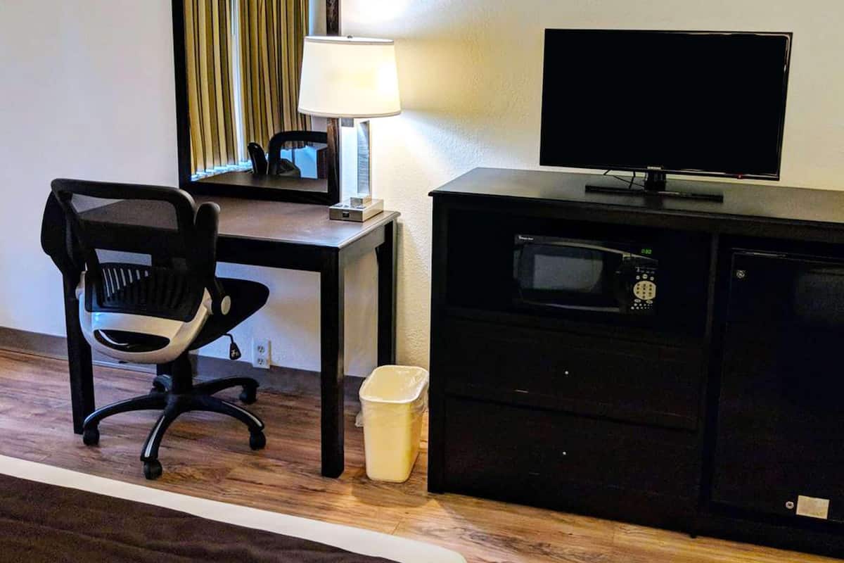 Hotellihuone, jossa on työpöytä, tuoli, televisio, mikroaaltouuni ja roskakori.