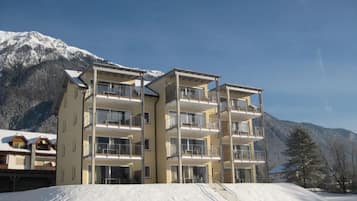 A multi-story hotel with balconies, set against a snowy mountain backdrop.