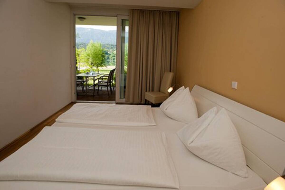 Hotelkamer met twee bedden, een balkon met een tafel en stoelen, en uitzicht op groen.