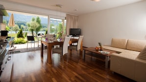 A modern living room with a wooden dining table, sofa, and a TV. - Appartements De Luxe Schluga (Hermagor-Pressegger See)