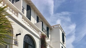 Un bâtiment blanc avec un escalier menant à un balcon, entouré de verdure et de fleurs.