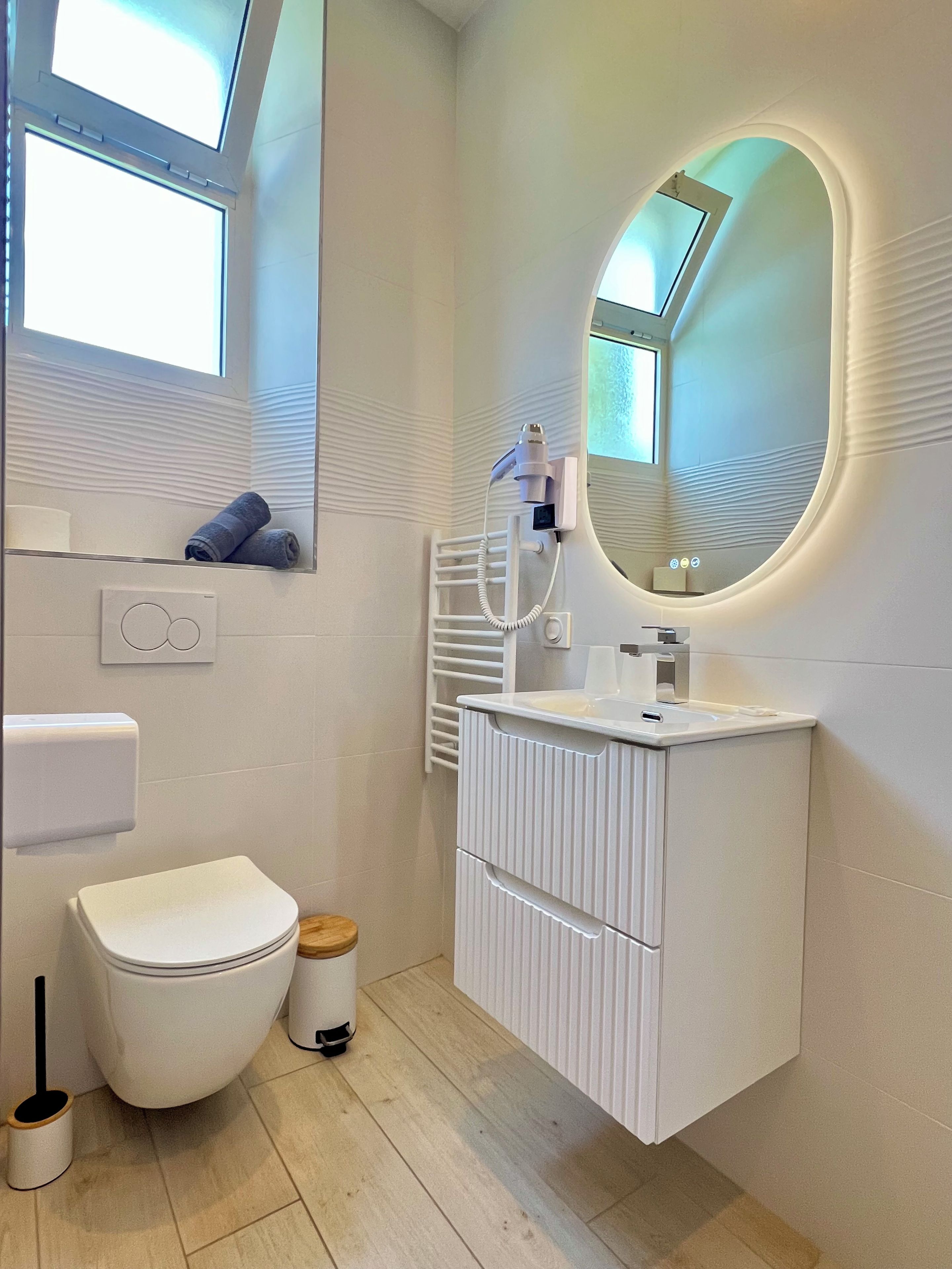 A modern bathroom with a toilet, bidet, vanity, and a large mirror with a built-in light.