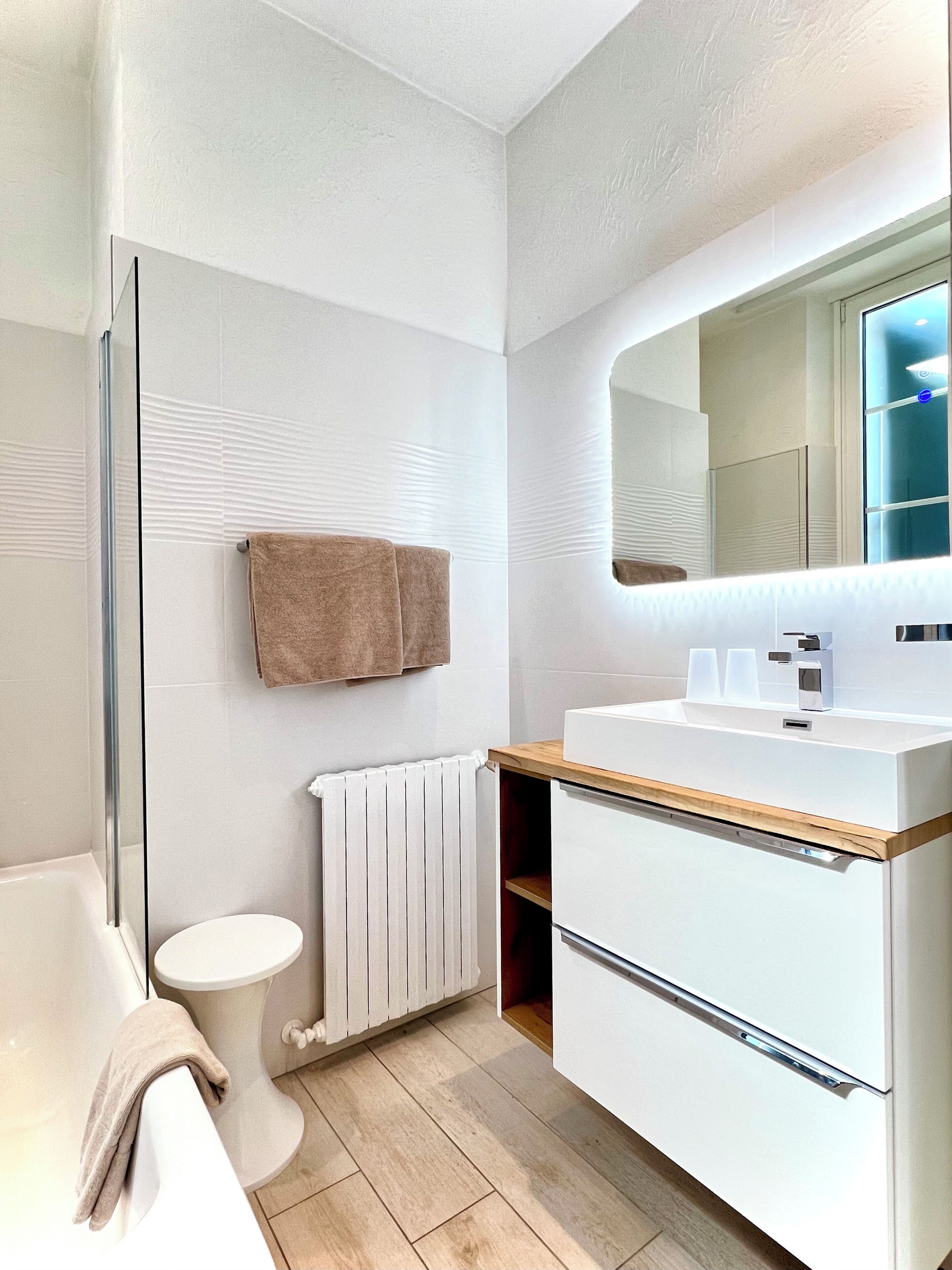 Un baño moderno con cabina de ducha de vidrio, inodoro blanco, lavabo blanco con encimera de madera y una toalla colgada en la pared.