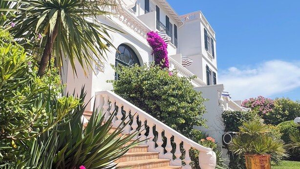 Un bâtiment blanc doté d’un balcon, d’un escalier en briques et de plantes en pot.