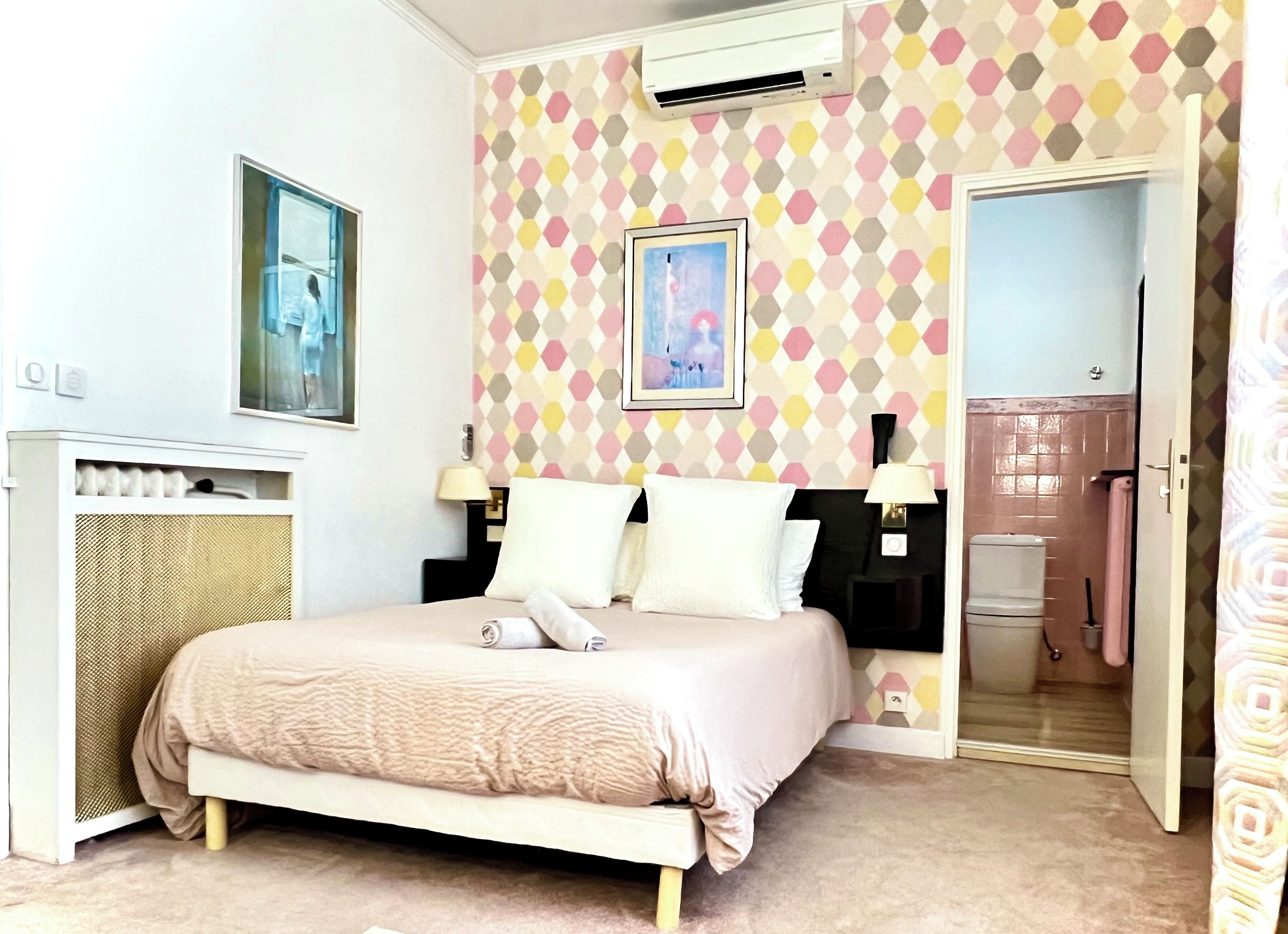 Camera da letto ordinata con un letto, comodini, condizionatore d'aria a parete e una porta che conduce al bagno.