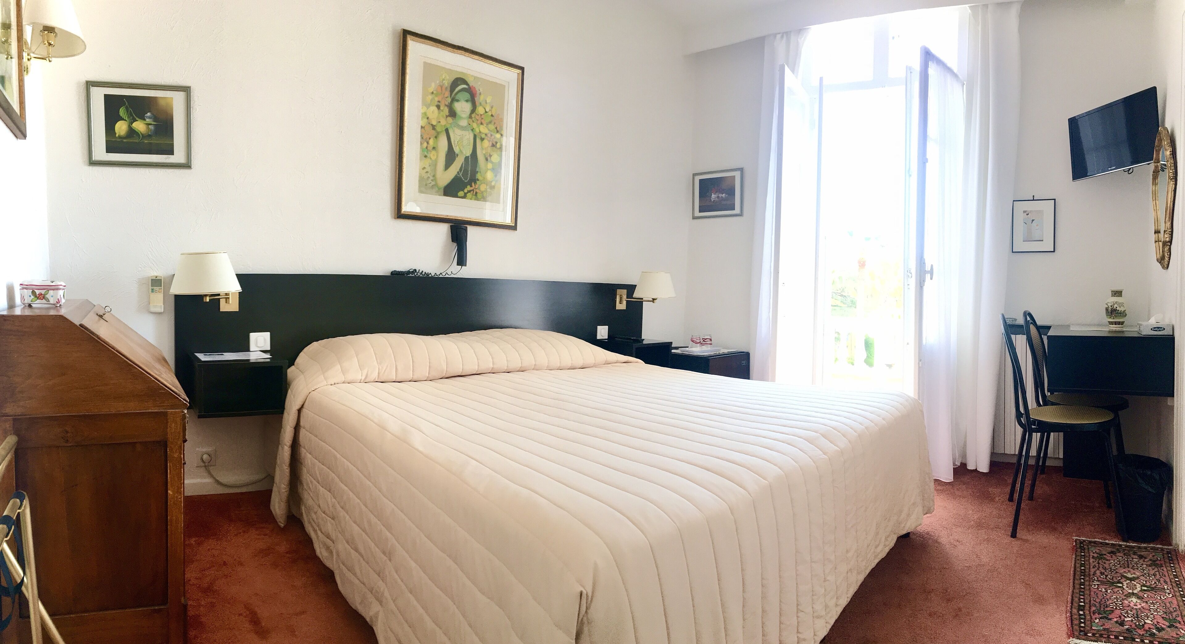A hotel room with a large bed, bedside tables, a desk, a chair, and a TV.