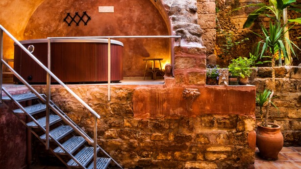 A stone-walled interior with a wooden bench, a staircase, and potted plants.