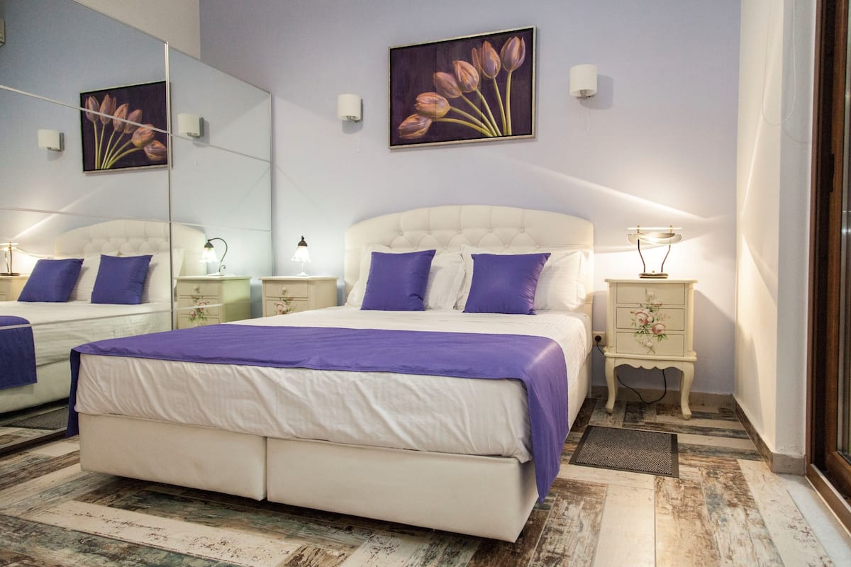 A bedroom with a large bed, two bedside tables, a nightstand, a mirror, and two wall-mounted lamps.