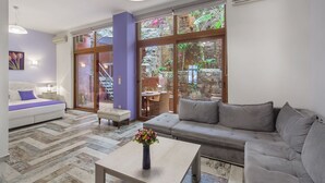 A modern living room with a sofa, a coffee table, and a view of a stone wall and greenery outside.