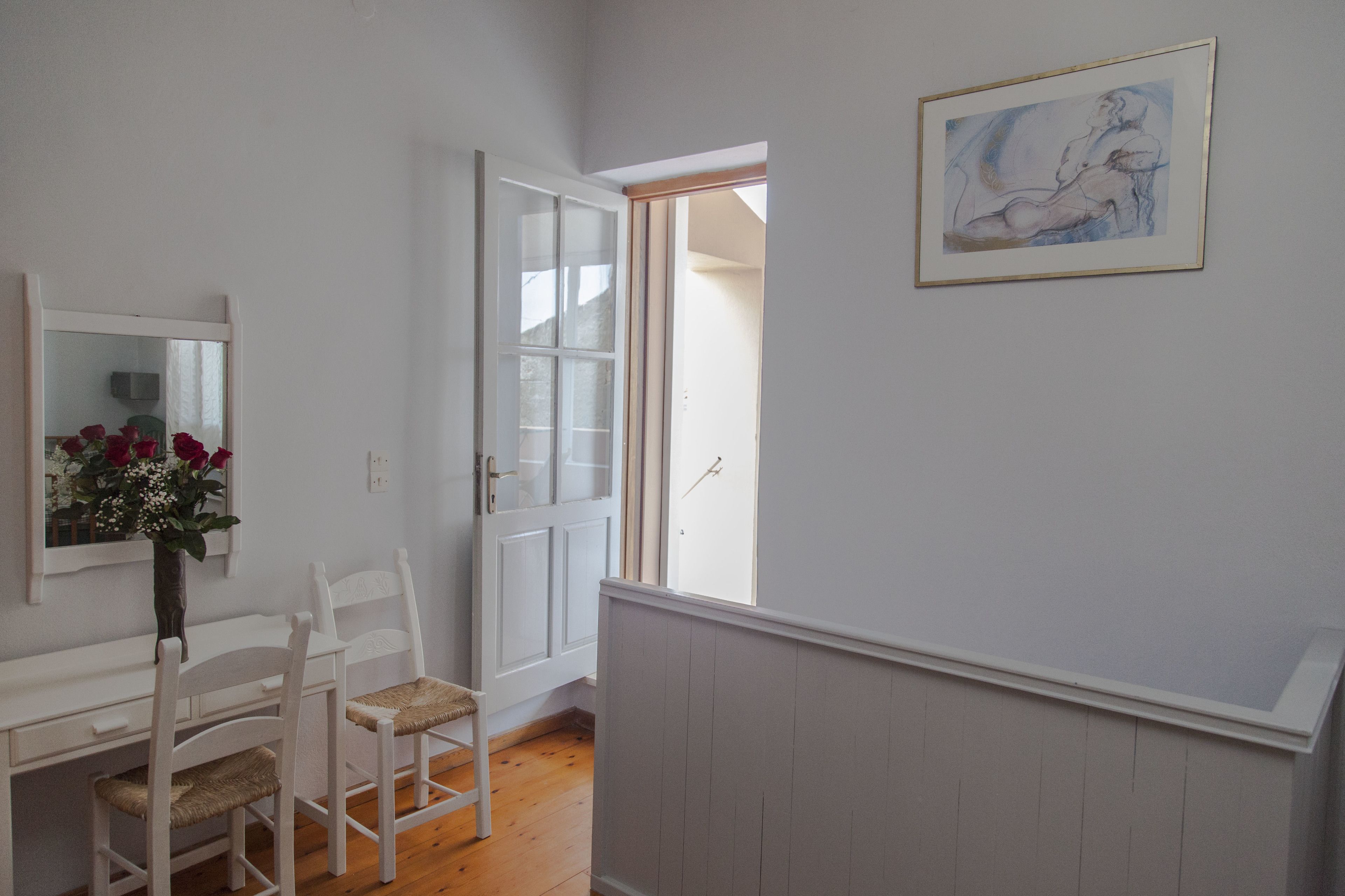 A room with a white desk, two chairs, a vase with flowers, a framed artwork, and a door leading to another room.