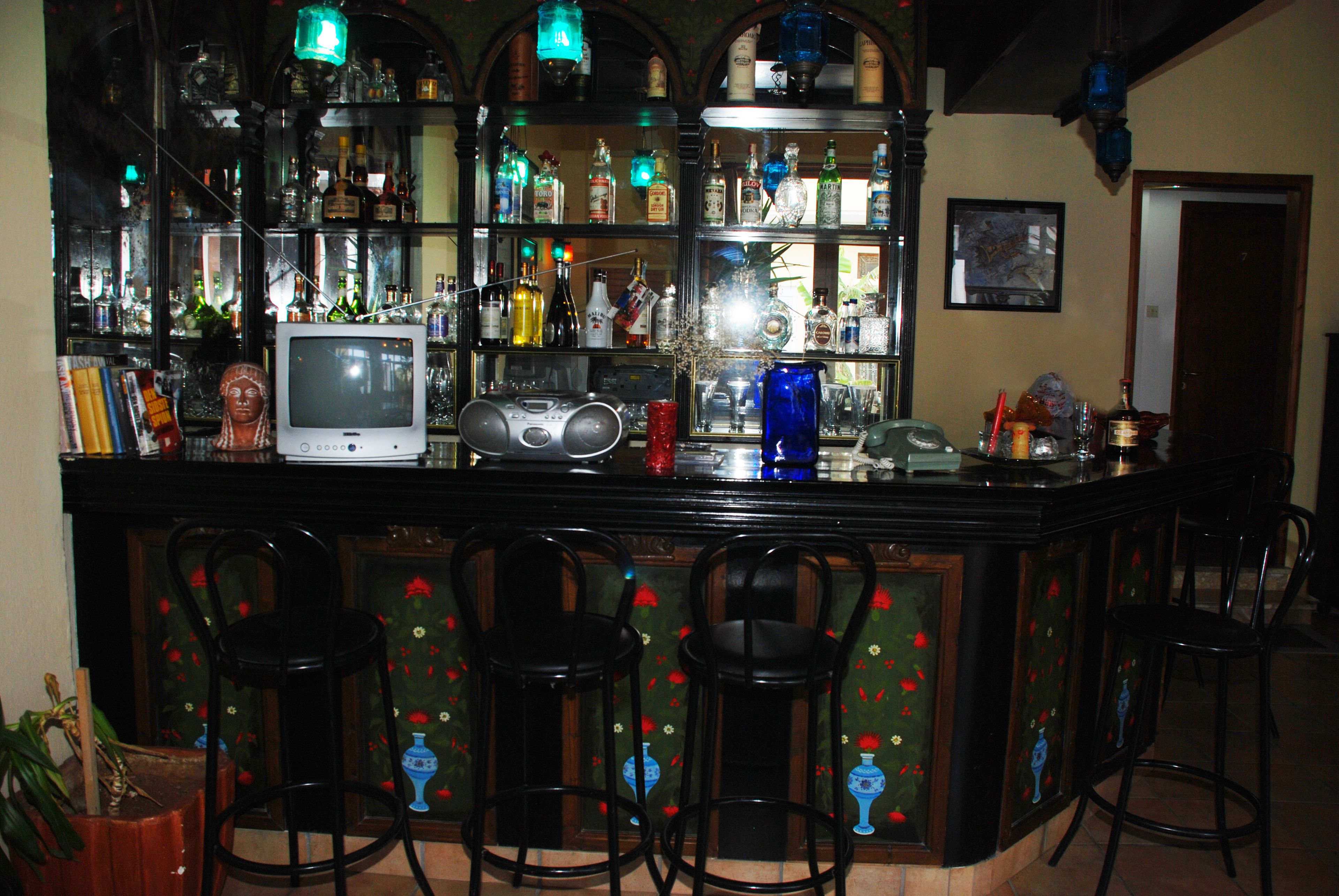 Zona de bar con televisor, estantes de botellas y cuatro taburetes.