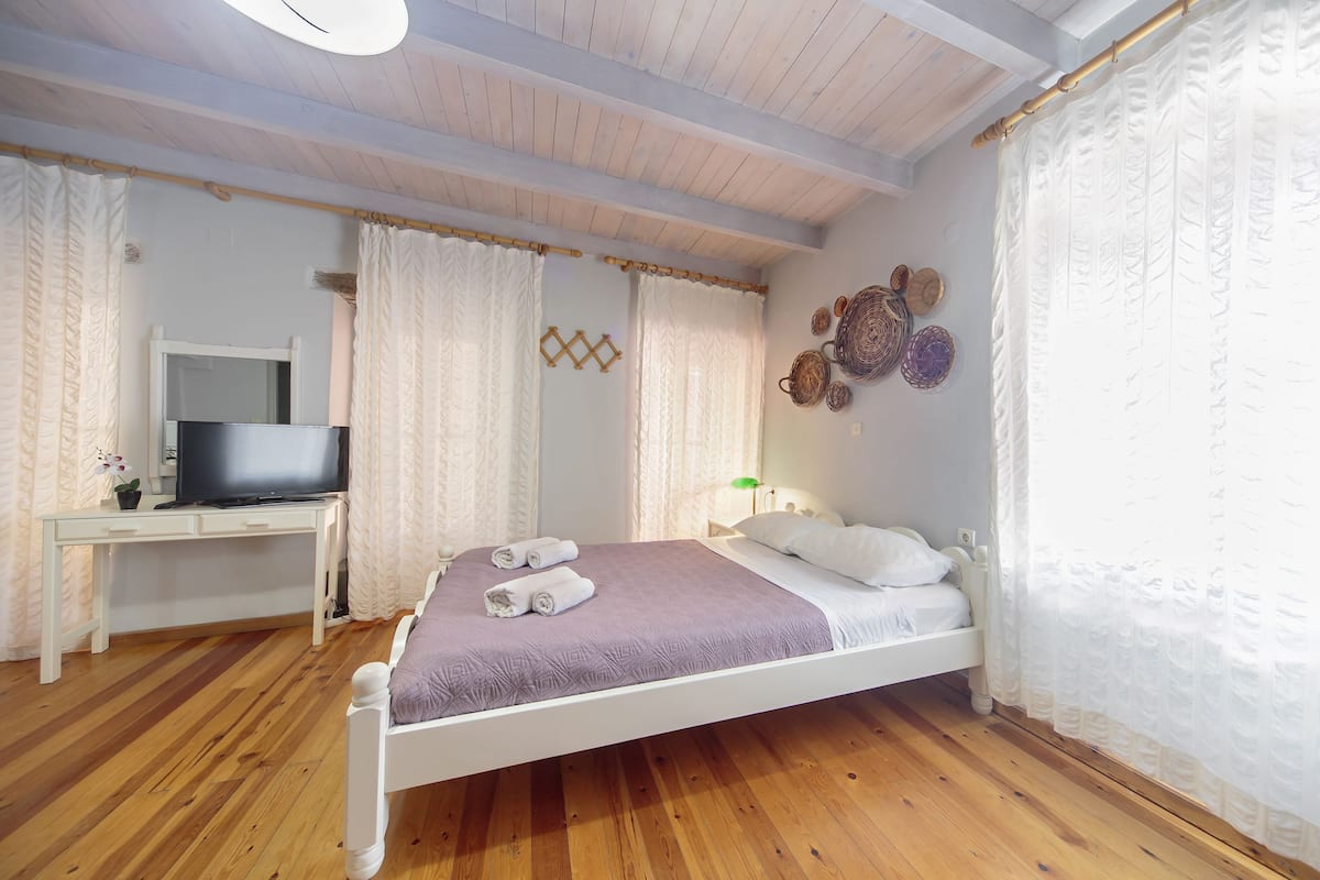 A bedroom with a bed, a desk, a television, and a wall-mounted lamp.