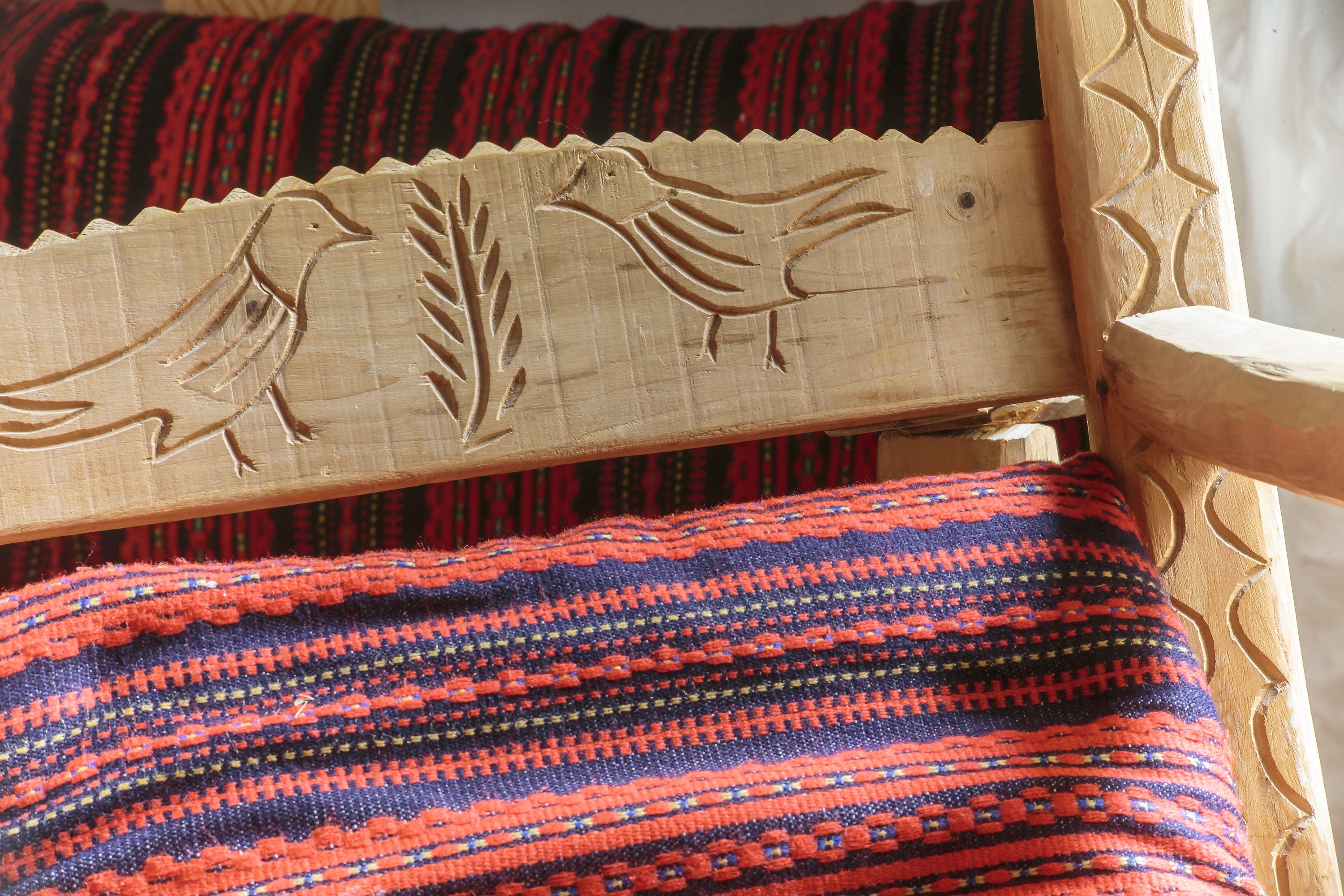 A wooden chair with carved birds and a woven fabric with a red, blue, and black pattern.