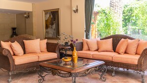 A living room with two brown wicker sofas, orange cushions, a glass coffee table, and a vase with flowers. - Ipek Garden Palace Residence - Boutique Class (Bodrum)