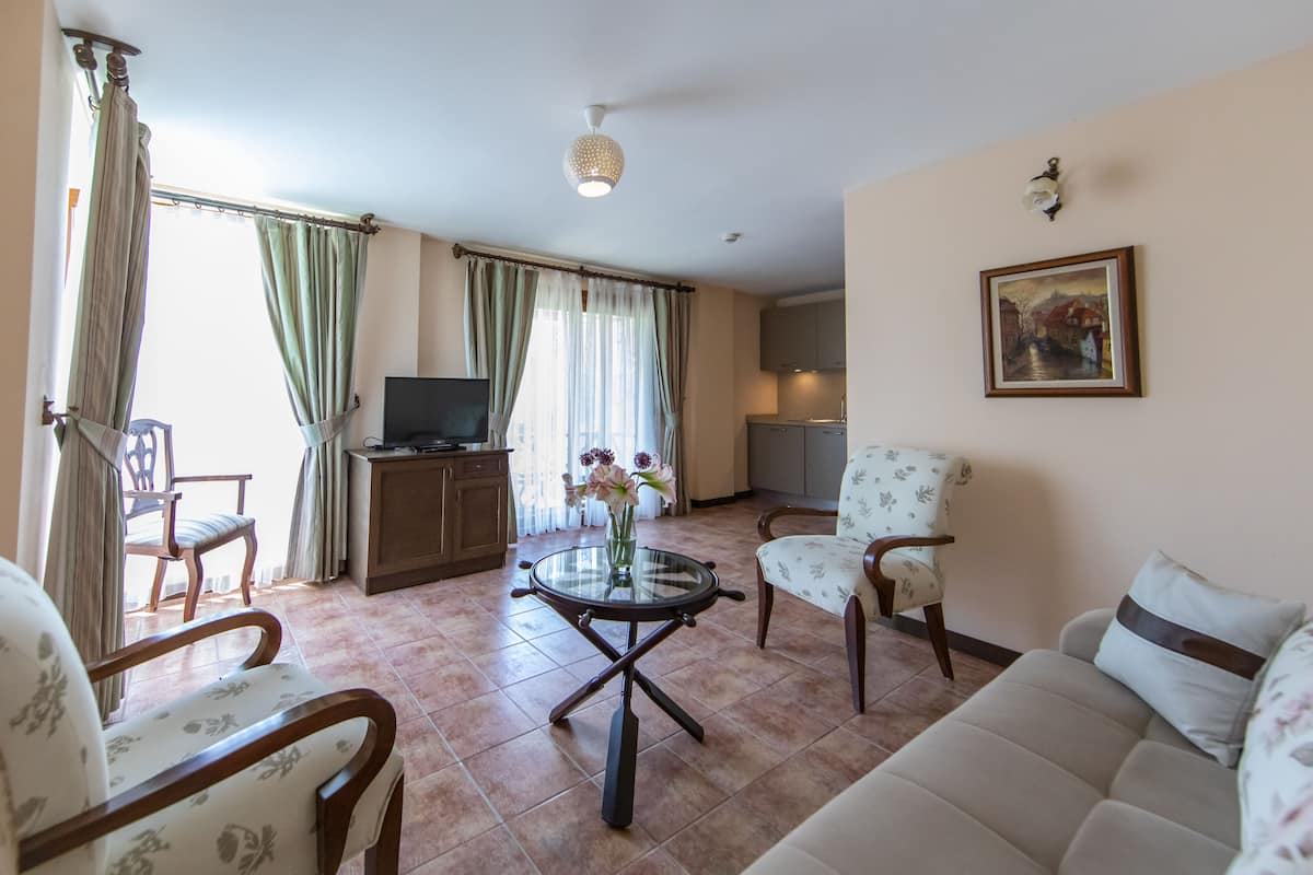 Un salon comprenant un canapé, des fauteuils, une table basse avec un plateau en verre, un téléviseur et un tableau accroché au mur.