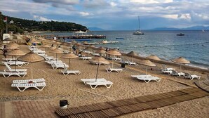 A beach with sun loungers and umbrellas, a pier, and boats in the water. - Ipek Garden Palace Residence - Boutique Class (Bodrum)