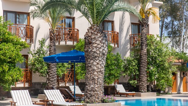 A pool area with lounge chairs, palm trees, and a building with balconies. - Ipek Garden Palace Residence - Boutique Class (Bodrum)
