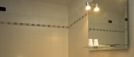 A bathroom with a white sink, toilet, and shower. There is a mirror above the sink and a towel rack with towels.