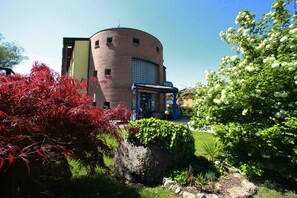 A hotel with a circular brick building, a covered entrance, and a well-maintained garden with red and white flowering plants.