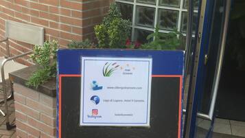 A signboard with the hotel's name and website, placed outside a building with a brick wall and a window.