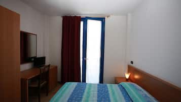 Habitación de hotel con cama, escritorio, silla, televisor, mesita de noche con lámpara y ventana con cortinas.