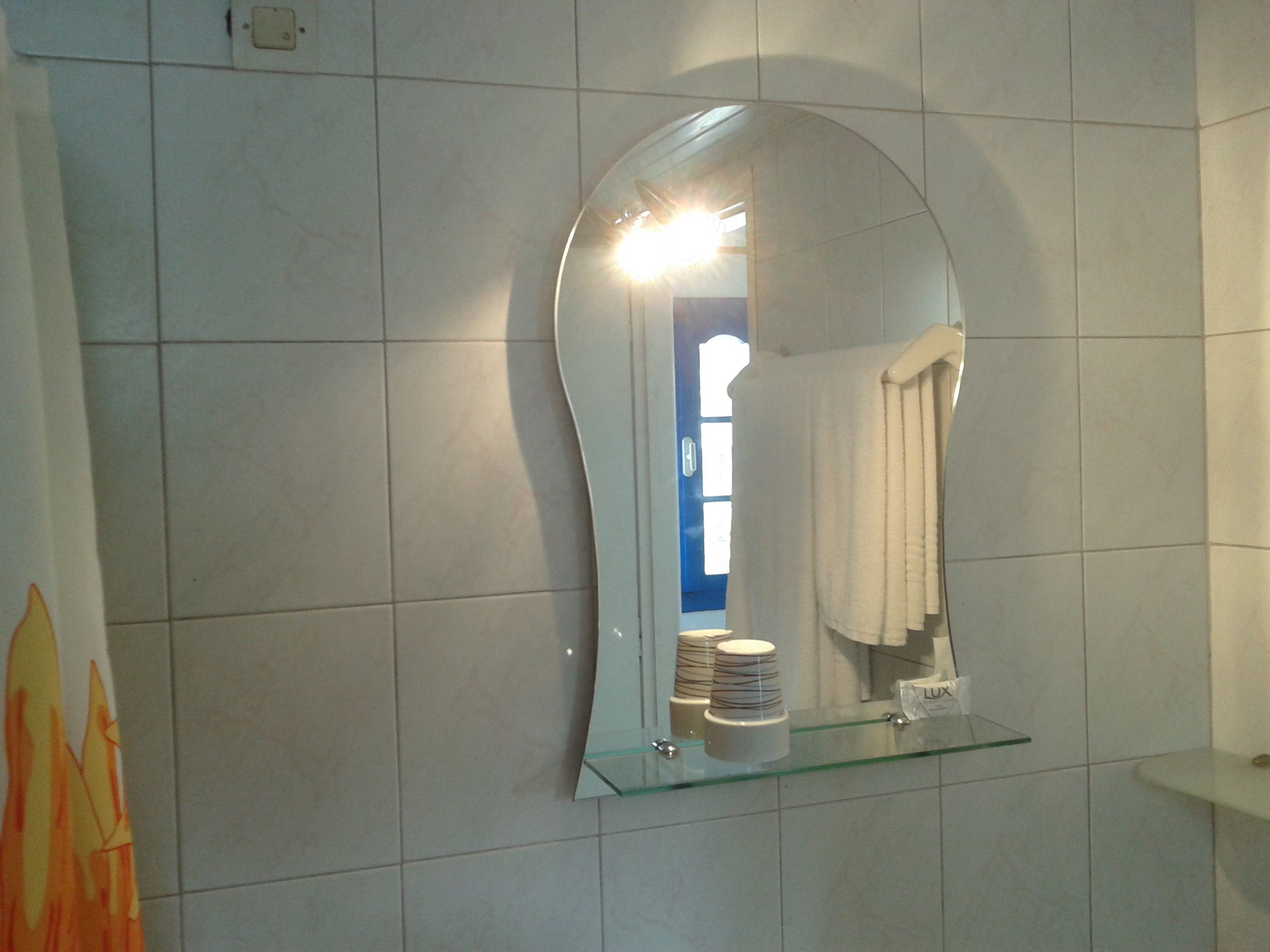 A bathroom with a large mirror, a glass shelf with toiletries, and a blue door in the background.