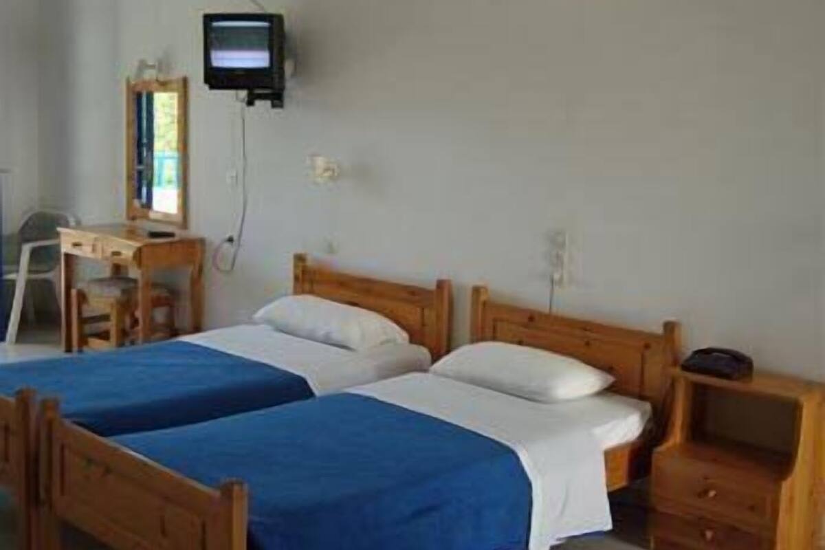 A simple room with two single beds, a desk with a chair, a television, and a small bedside table.