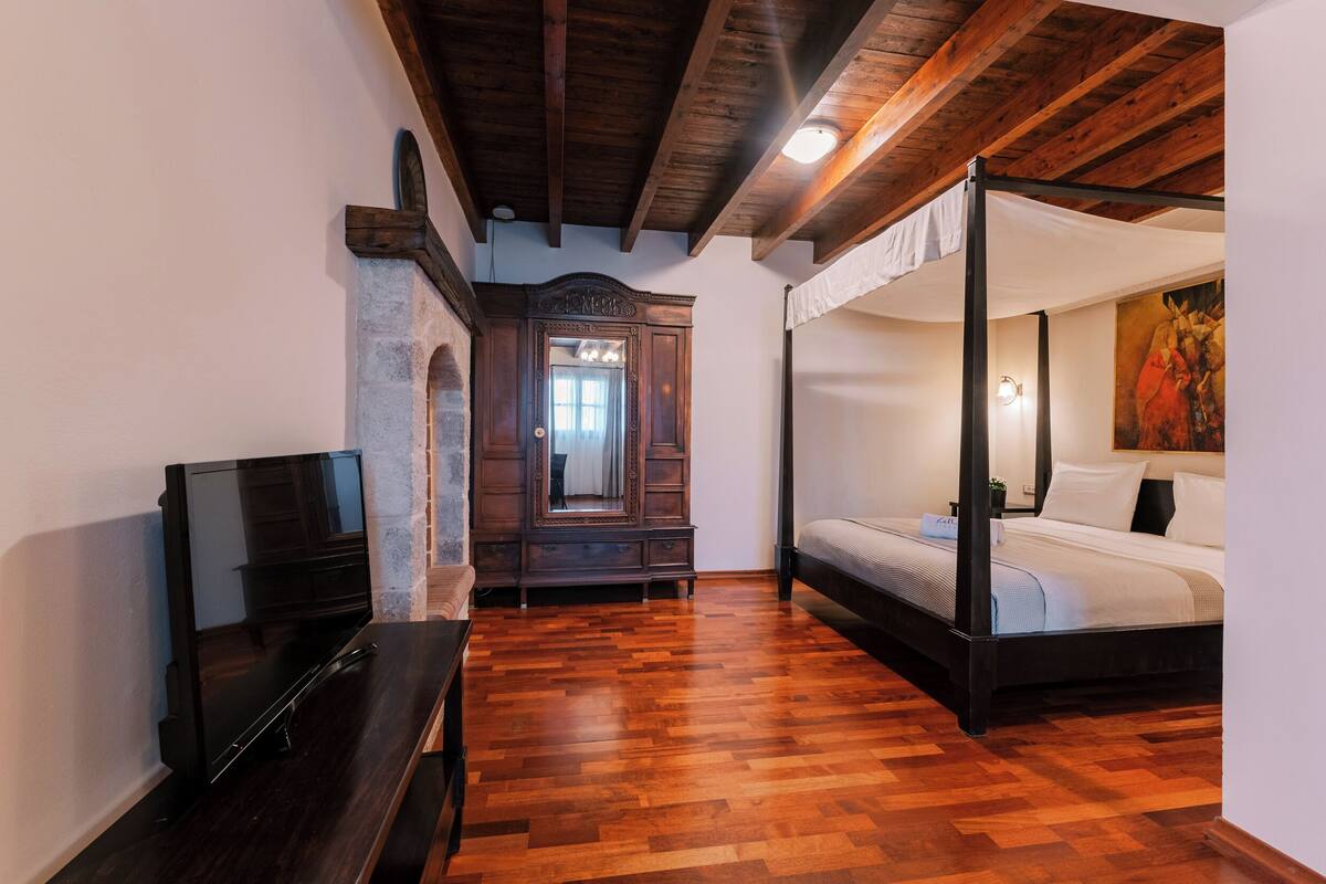 A bedroom with a four-poster bed, a television, and a stone fireplace.