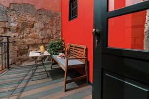Un pequeño espacio al aire libre con una mesa, un banco de madera, una puerta y un muro de piedra.