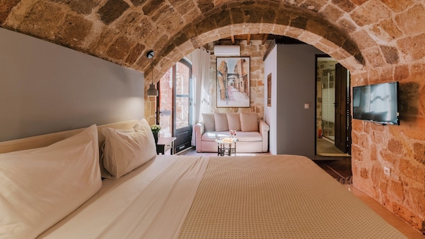 A bedroom with a stone archway, a bed, a sofa, a TV, and a painting on the wall. - Zacosta Villa - a Heritage Hotel (Rhodes)