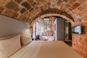 A bedroom with a stone archway, a bed, a sofa, a TV, and a painting on the wall. - Zacosta Villa - a Heritage Hotel (Rhodes)