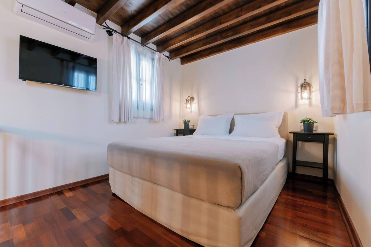 A bedroom with a large bed, wooden flooring, a mounted TV, and two bedside tables with lamps.