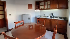 A dining area with a round table and four chairs, a refrigerator, and wooden cabinets in a kitchen. - Travelers Apartamentos & Suites Castellón de Juanambú (Cali)