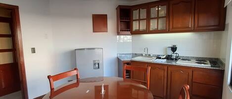 Un comedor con una mesa redonda y cuatro sillas, un refrigerador y armarios de madera en una cocina.
