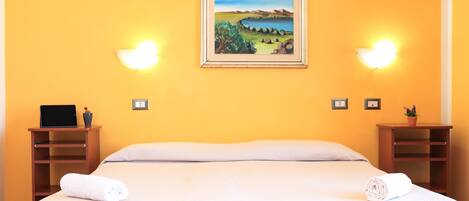 Una habitación de hotel con cama, dos mesitas de noche, un cuadro y apliques de pared.
