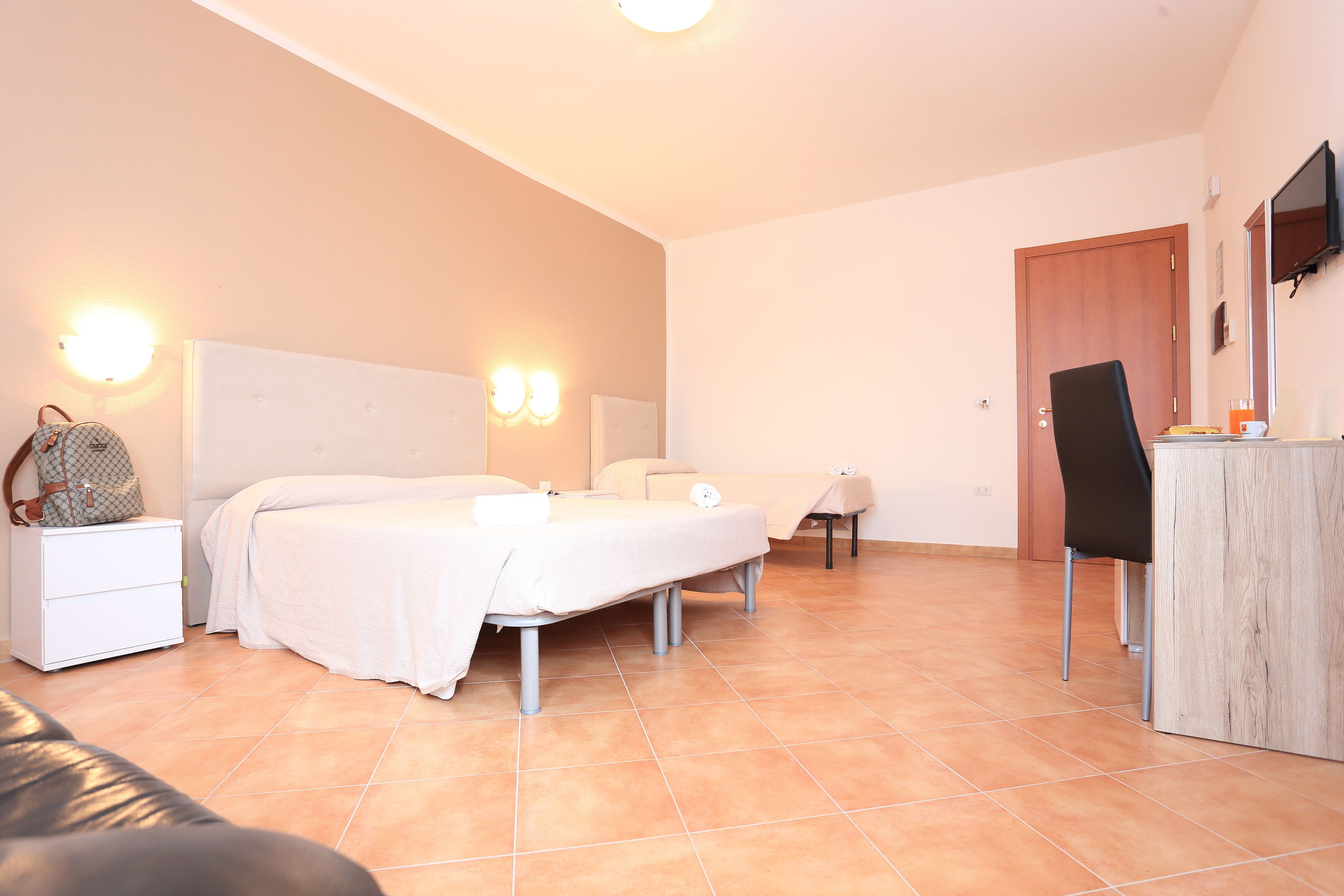 Une chambre avec deux lits, une table de chevet, une chaise, un bureau et un téléviseur fixé au mur.