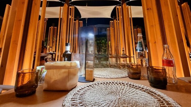 A cozy, tent-like interior with a woven mat at the center, wooden beams, and a glass table with drinks and bottles. - Hotel Villa Piras (Alghero)