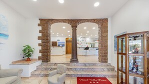 A hotel lobby with a stone archway, a reception desk, a bar area, and a glass display cabinet. - Hotel Villa Piras (Alghero)