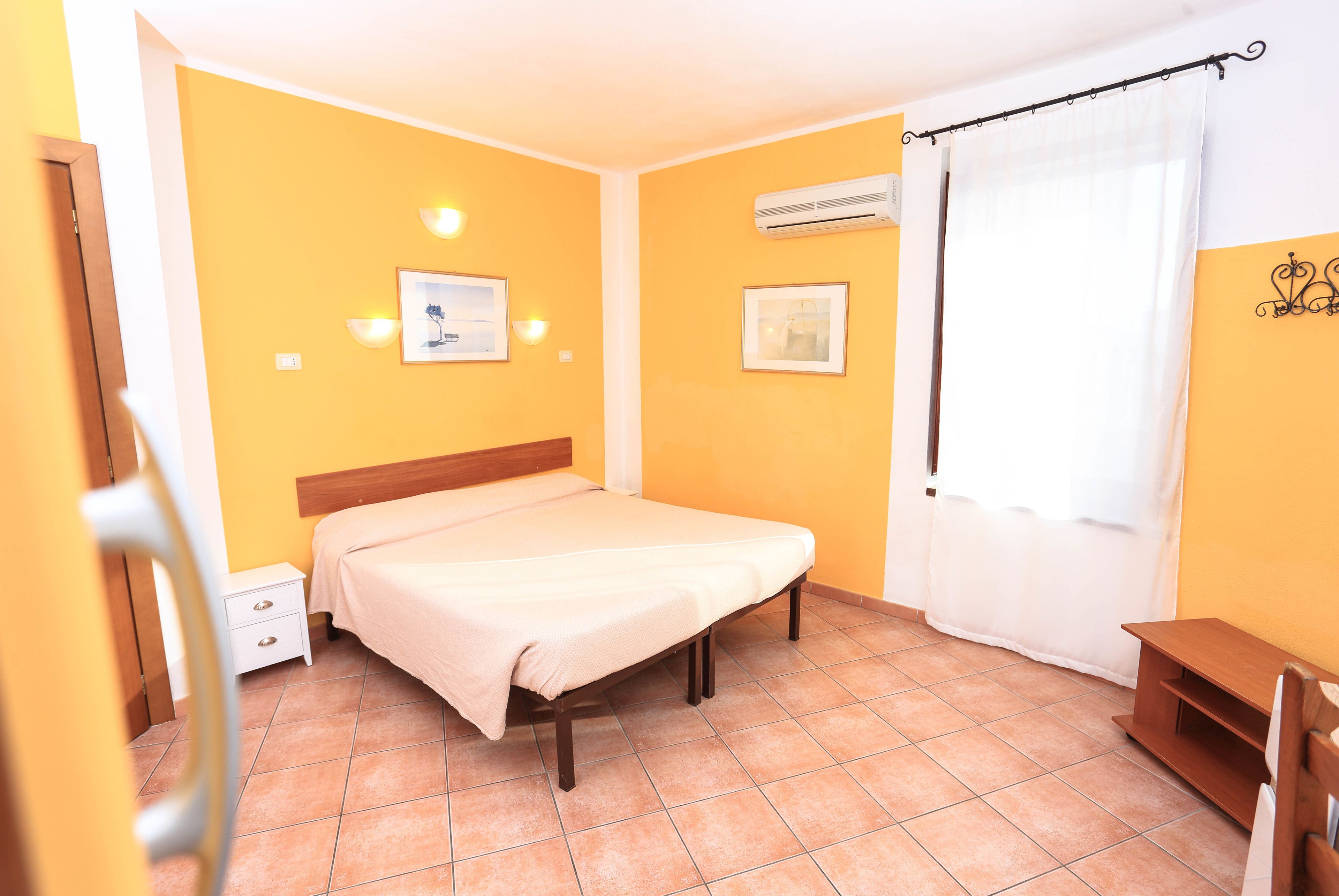 A bedroom with a bed, a nightstand, a wall-mounted air conditioner, and a window with a curtain.