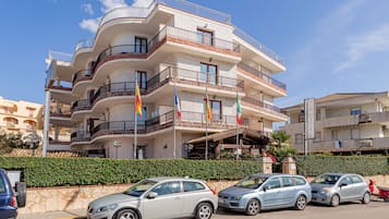 Hotel com vários andares, varandas, bandeiras e área de estacionamento.