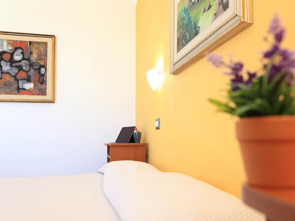 A hotel room with a bed, a nightstand with a laptop, a wall-mounted light, and a painting.