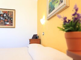 A hotel room with a bed, a nightstand with a laptop, a wall-mounted light, and a painting.