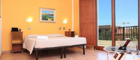 A bedroom with a bed, a bedside table, a nightstand, a window with a view, and a bottle of wine on a table.