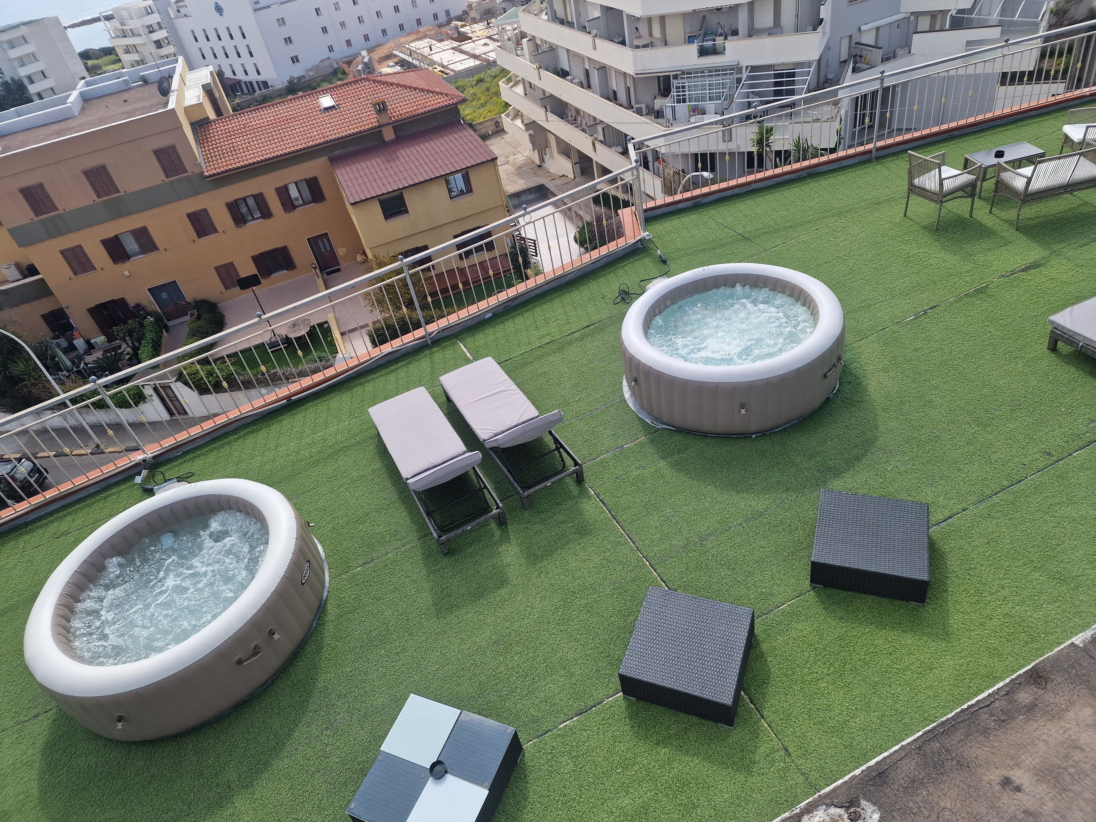 Eine Dachterrasse mit zwei Whirlpools, Liegestühlen und einem kleinen Tisch.