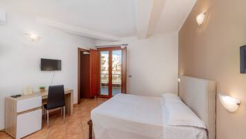 A hotel room with a bed, a desk with a chair, a television, and a balcony door.