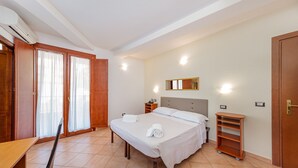 A bedroom with a bed, a desk, a chair, a wardrobe, and a small shelf unit. - Hotel Villa Piras (Alghero)