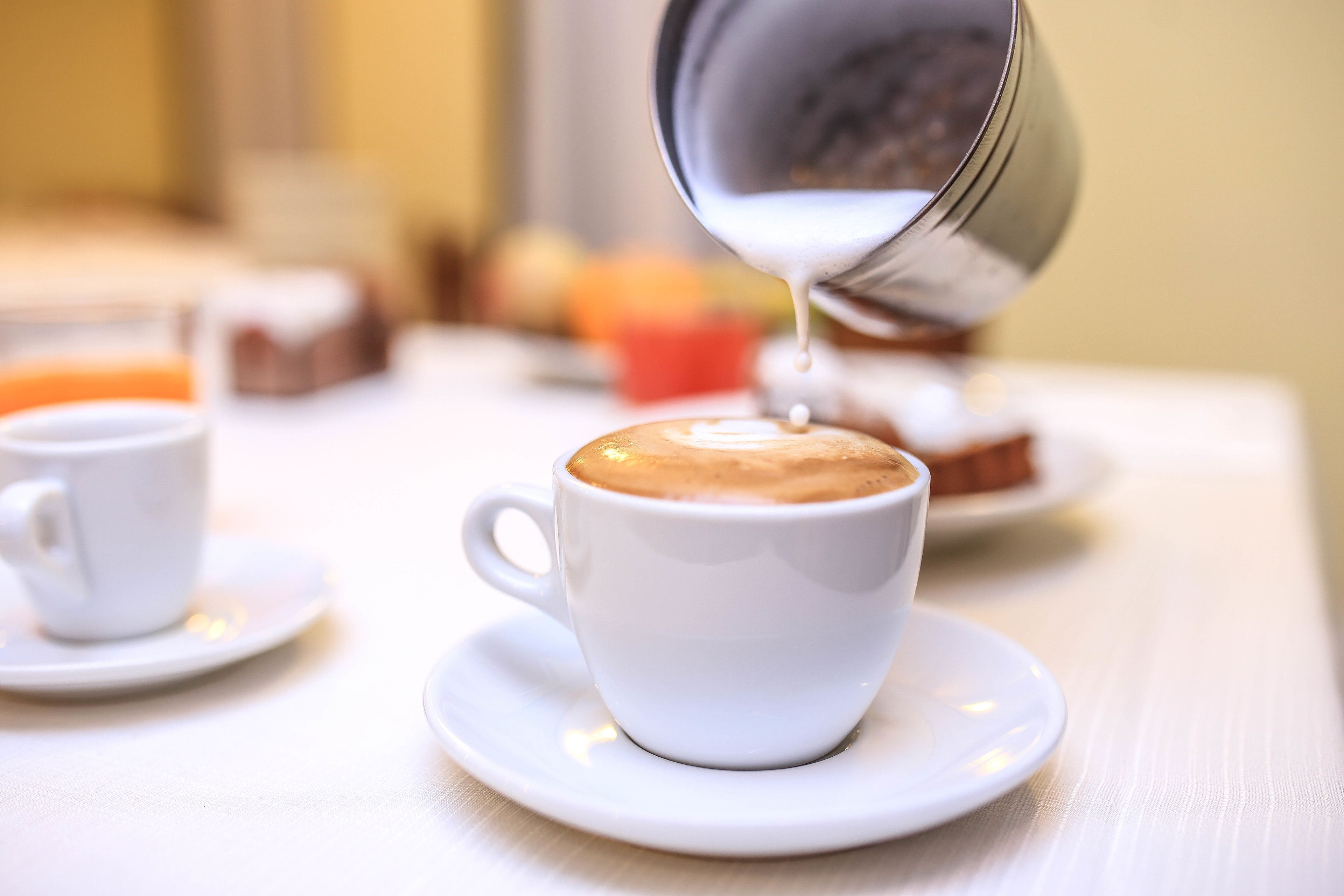 A white cup of coffee with a saucer on a table.